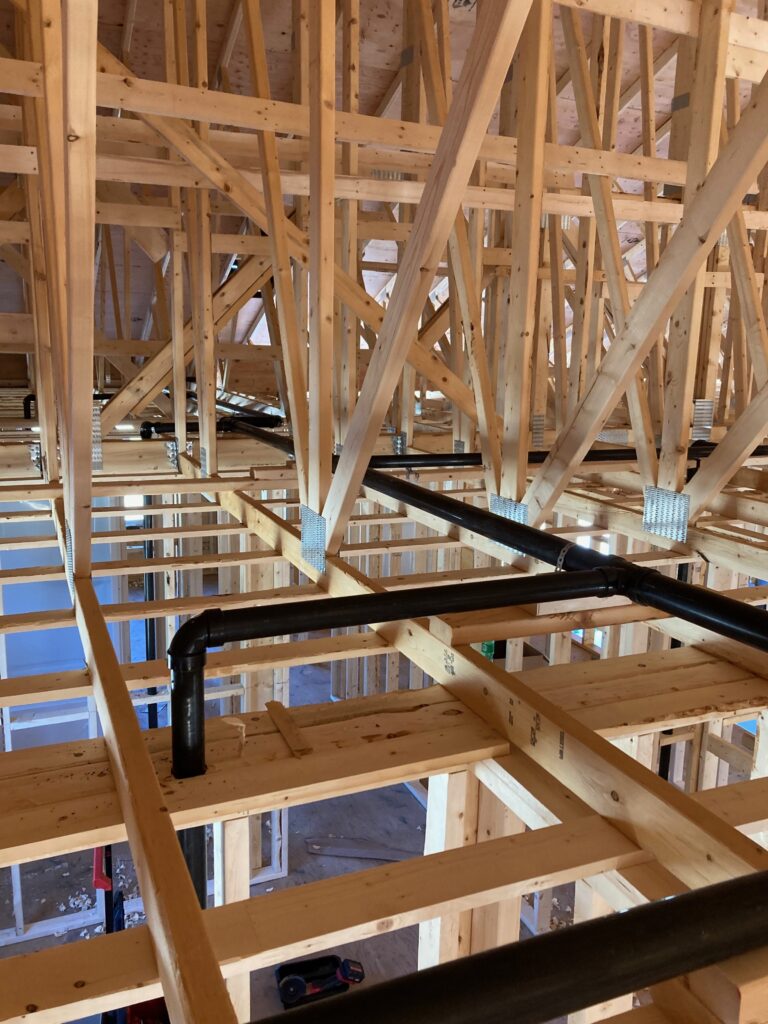 Residential plumbing rough-in showing ABS drain pipe installation through floor trusses in new construction home in St. John's, NL